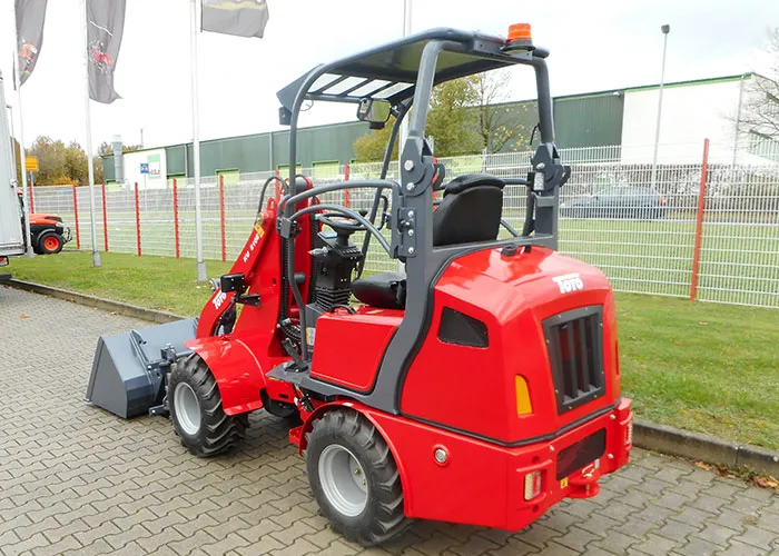 Toyo Hoflader Modell 810E mit Bügel – Heckansicht mit Schaufel, Überrollbügel und Rundumleuchte, auf Hofpflaster vor Zaun