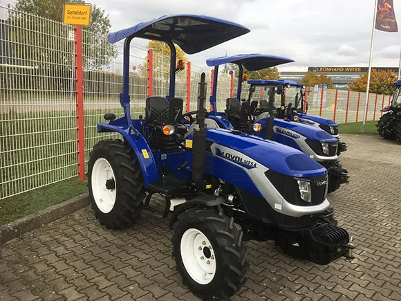 Lovol Traktor Modell M254 Stage V mit Bügel – Seitenansicht von vorne links, mit Sonnendach, auf Verkaufsgelände vor Zaun