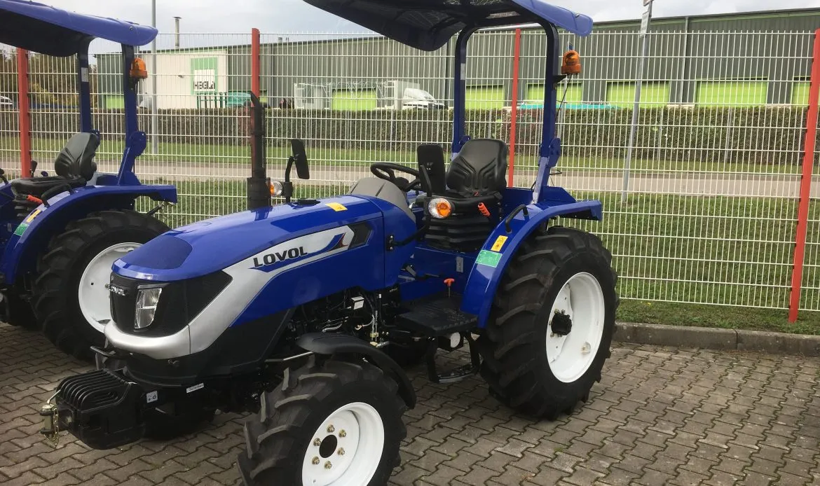 Lovol Traktor Modell M404 Stage V mit Bügel – Seitenansicht links, mit Überrollbügel und Sitz, auf Hofplatz vor Zaun
